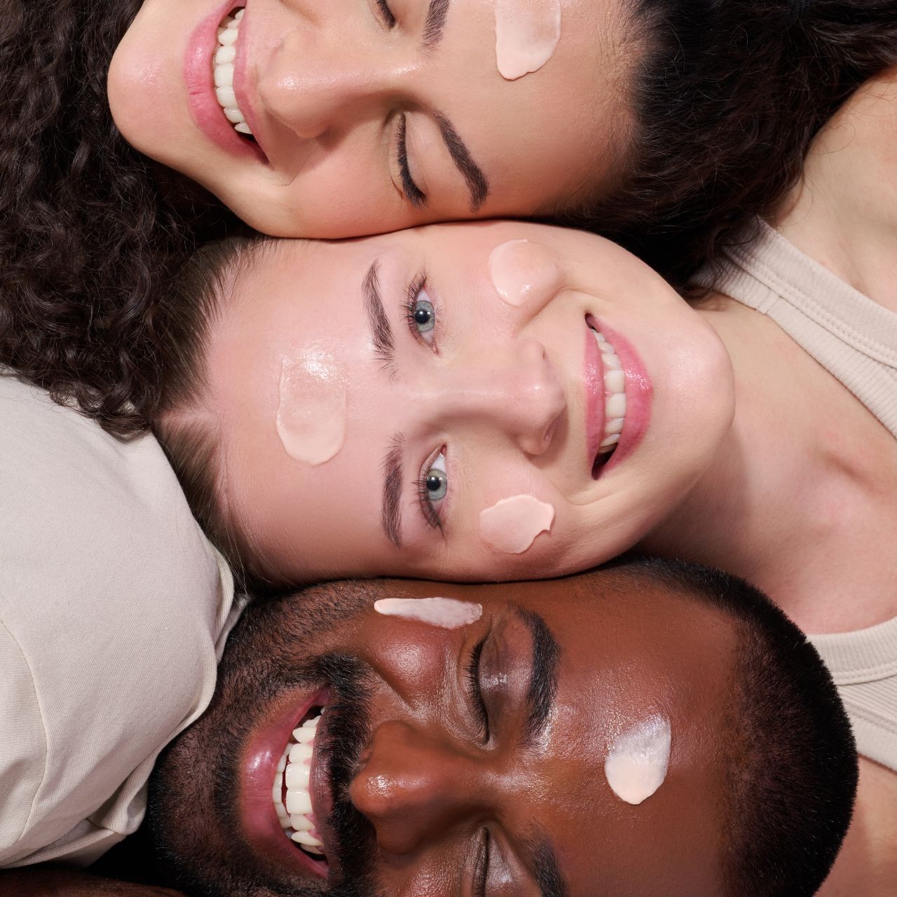 Drei lächelnde Menschen liegen mit Gesichtsmasken nebeneinander, glücklich und entspannt.