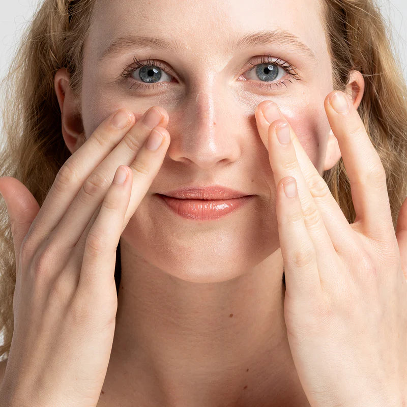 Frau massiert ihre Wangen mit den Fingerspitzen, blickt direkt in die Kamera und hat leicht lächelnde Gesichtszüge.
