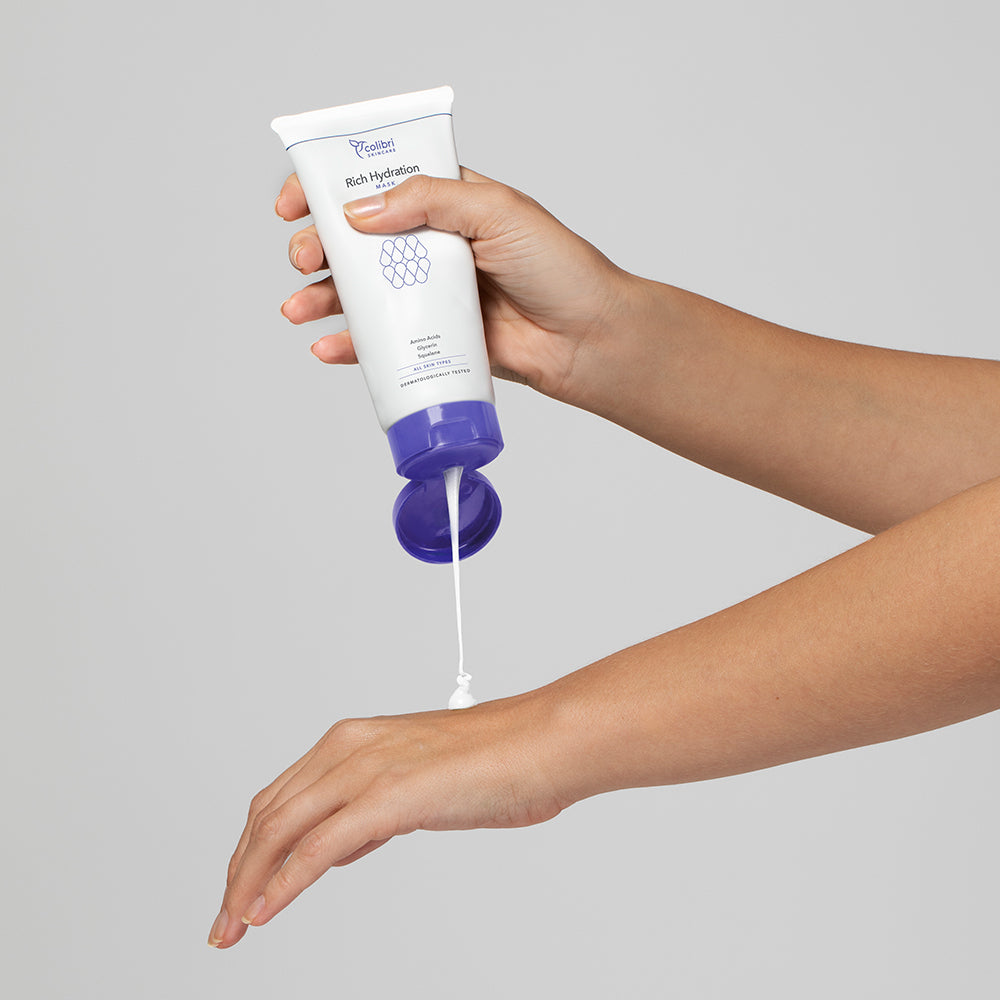 Eine Person trägt weiße Lotion aus einer Tube mit lila Kappe auf ihren Unterarm auf.
