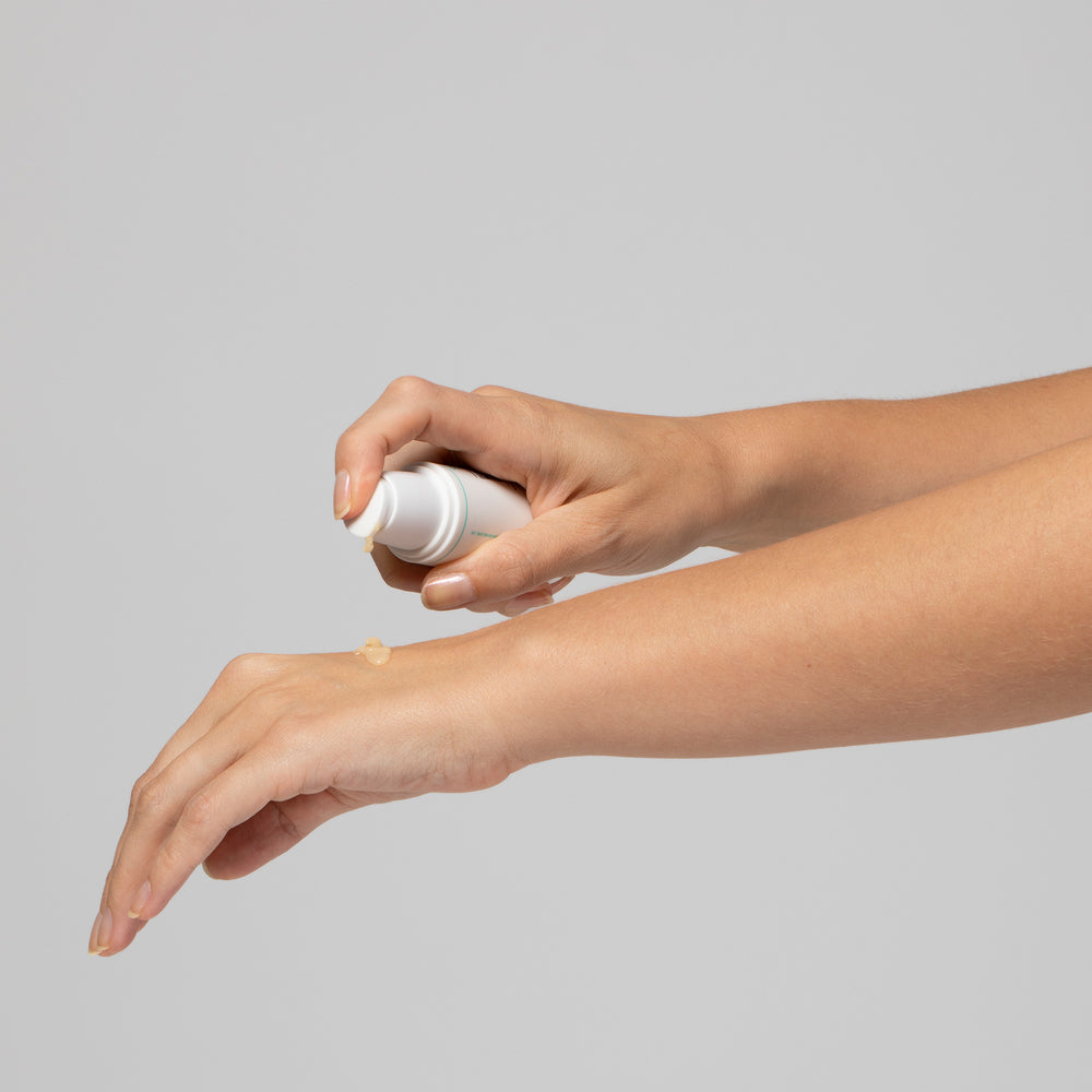 Eine Hand trägt Creme aus einem weißen Spender auf den Unterarm einer anderen Hand auf.