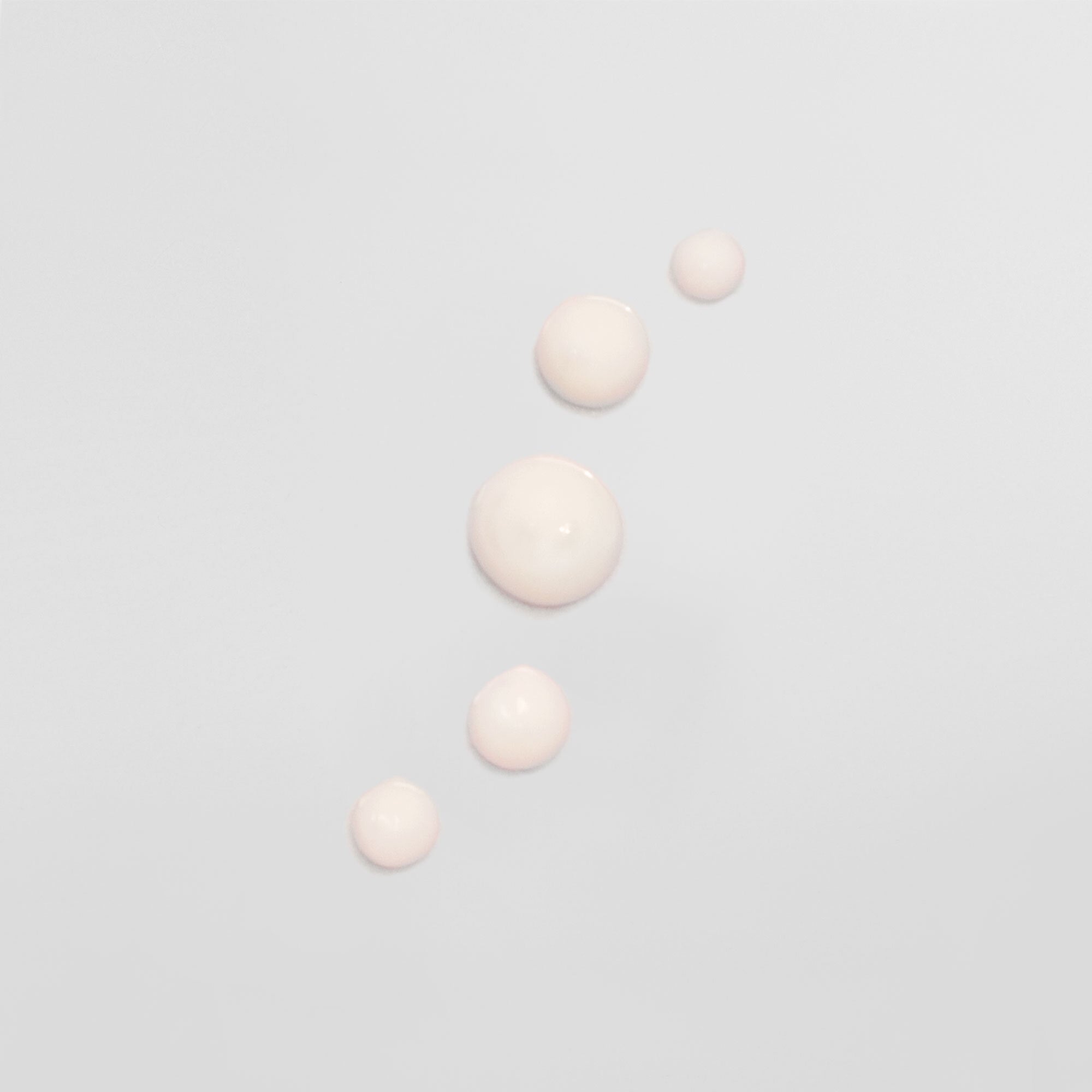 Fünf cremefarbene Tropfen auf einem hellgrauen Hintergrund, in einer diagonalen Linie angeordnet.