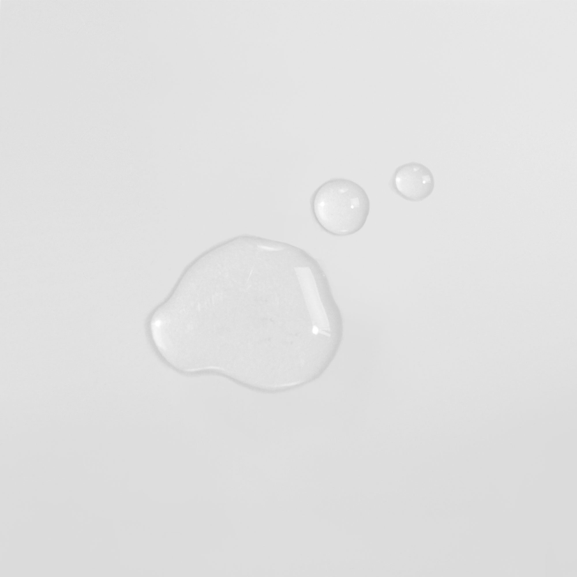 Drei Wassertröpfchen auf einer weißen Oberfläche, zwei kleinere oben rechts und ein größeres links unten.