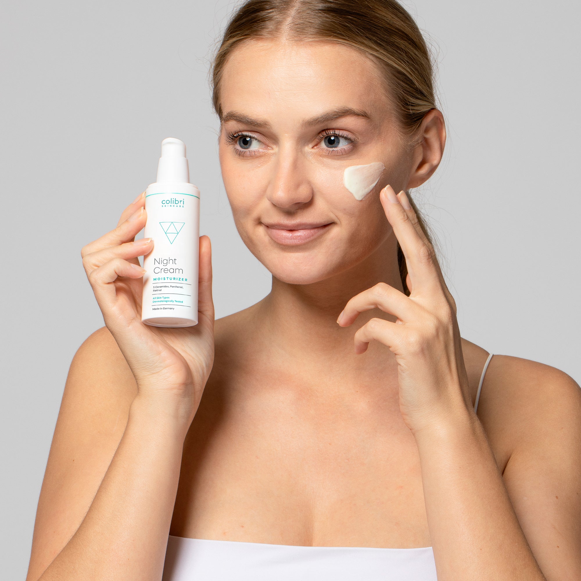 Frau trägt Nachtcreme auf Wange auf und hält die Cremedose in der anderen Hand.