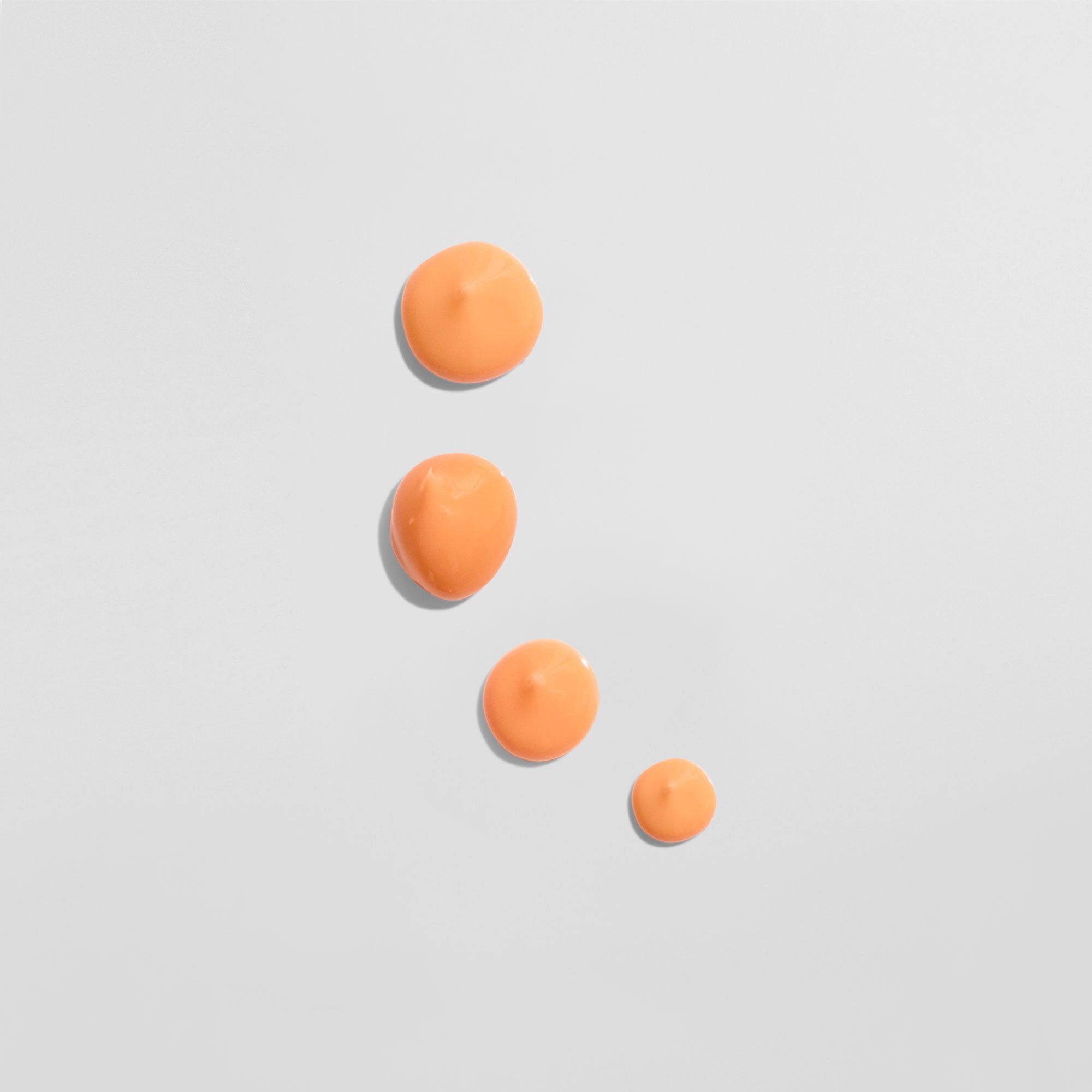 Vier orange Farbtropfen auf einer weißen Oberfläche in einer absteigenden Anordnung.
