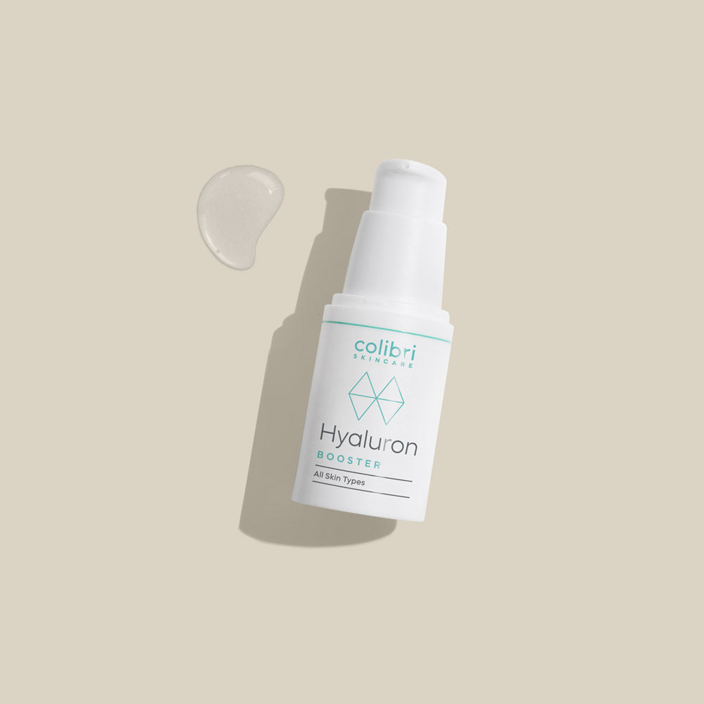 Flasche mit Hautpflegeprodukt namens „Hyaluron Booster“ auf beige Hintergrund, daneben ein Tropfen des Produkts.