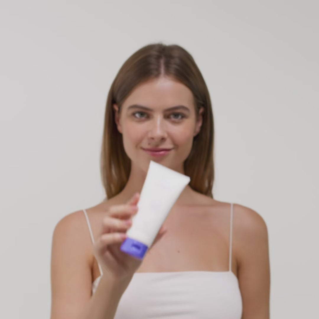 Eine Person hält eine Tube, vermutlich mit Kosmetikprodukt, in der Hand und lächelt leicht.