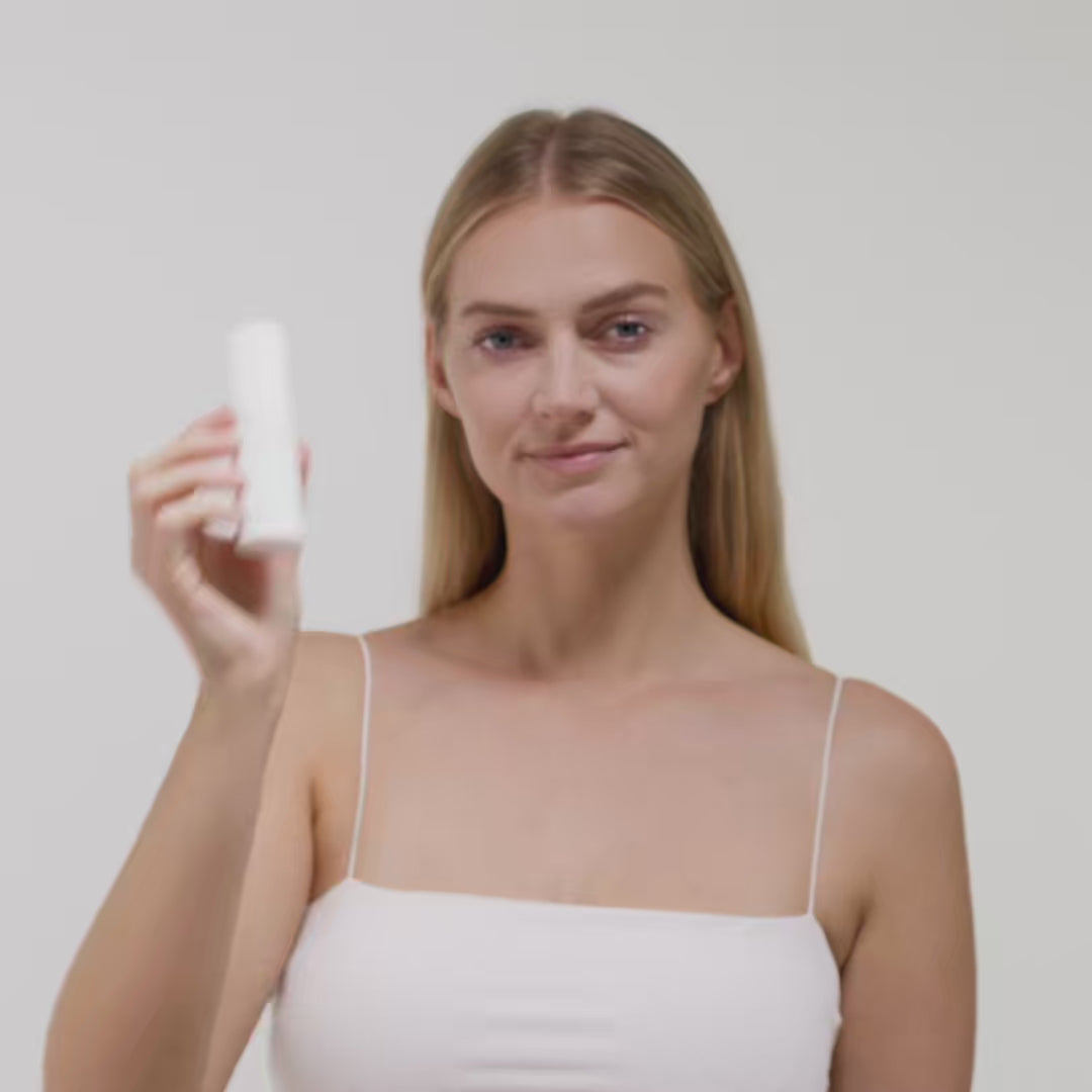 Frau in einem weißen Top hält einen weißen Zylinder vor einem weißen Hintergrund in der Hand.