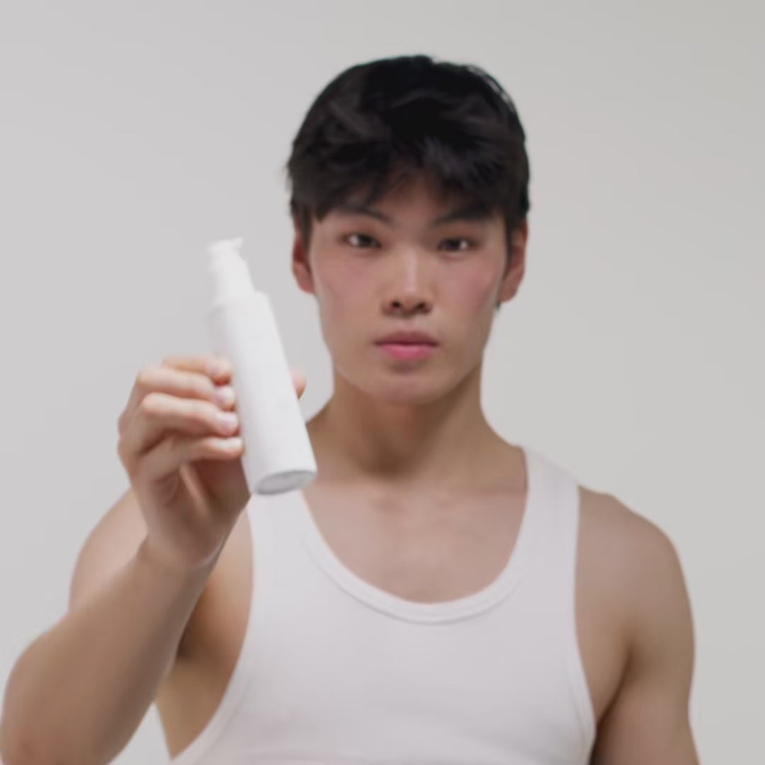 Ein Mann in einem weißen Tanktop hält eine weiße Flasche mit Spender in die Kamera.