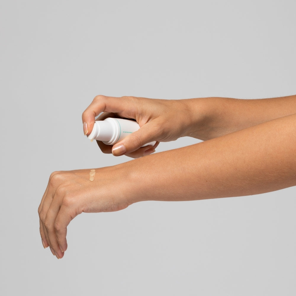 Eine Person trägt mit einem Pumpspender eine kosmetische Creme auf den Handrücken auf.