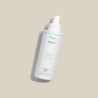 Weiße Flasche Aloe Vera Spray mit Wassertropfen auf beigem Hintergrund, leicht geneigt stehend.