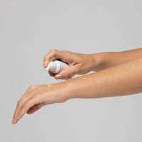 Eine Hand trägt Creme aus einem weißen Spender auf den Unterarm einer anderen Hand auf.