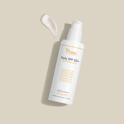 Flasche eines Feuchtigkeitscremes mit SPF 50+ auf beigem Hintergrund, daneben ein Klecks der Creme.