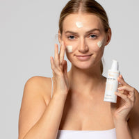 Eine Frau trägt Sonnencreme auf das Gesicht auf und hält eine Flasche mit der Aufschrift "Daily SPF 50+" in der Hand.